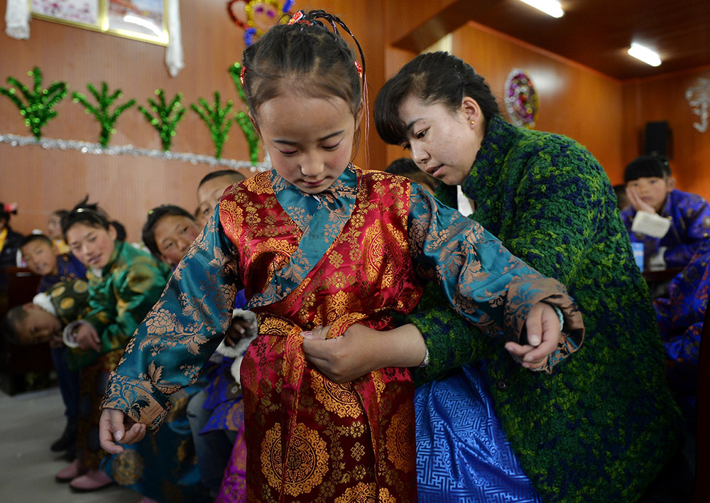 2月27日，在西藏自治区儿童福利院，来自拉萨市尼木县的“爱心妈妈”德庆旺姆（右）在为来自那曲地区的嘎玛曲宗换上节日盛装。